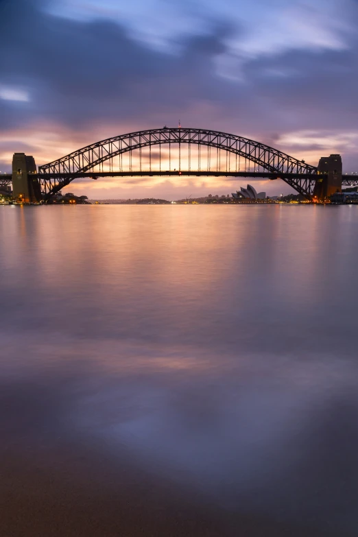 a bridge going over water at dusk with a sky line in the background
