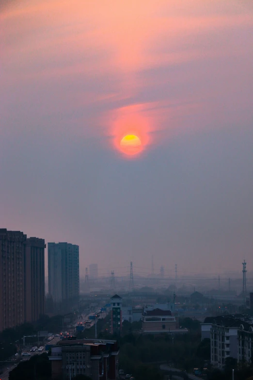 an orange and yellow sun behind tall buildings