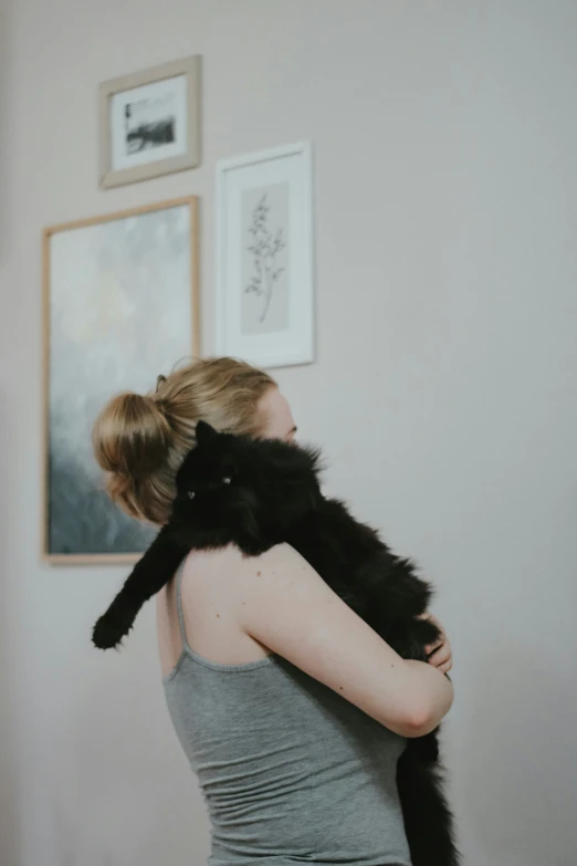 a woman holding a cat while wearing a gray tank top