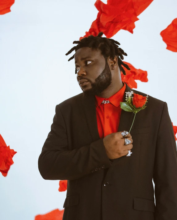 a man wearing a black suit and red tie holding a flower