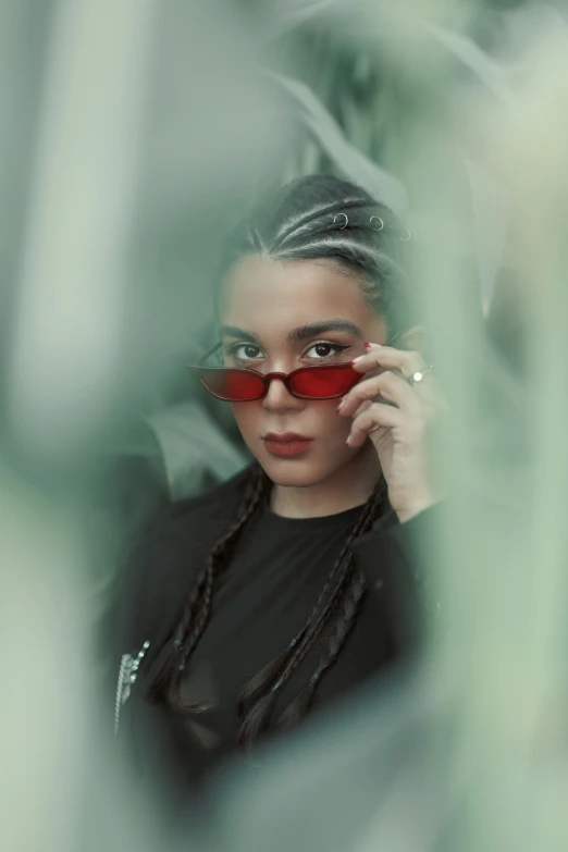 a woman wearing sunglasses looks through the leaves of plants