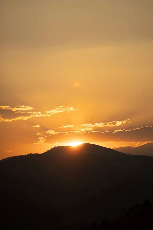 the sun sets behind the mountains in a cloudy sky