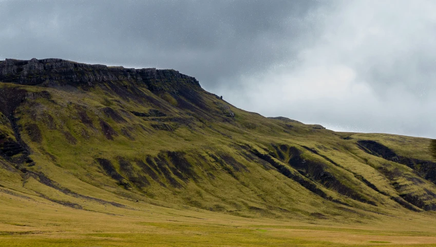 green grass field with cloudy sky above the hills