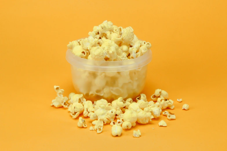 a plastic bowl filled with popcorn sitting on top of a orange surface