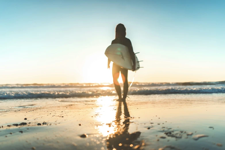 person walking on beach with surfboard at sunset