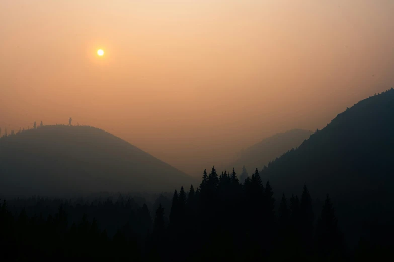 the sun is setting over a mountain on a hazy day