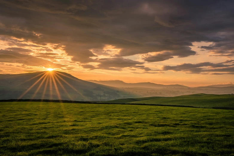 the sun setting over a grassy valley and mountains