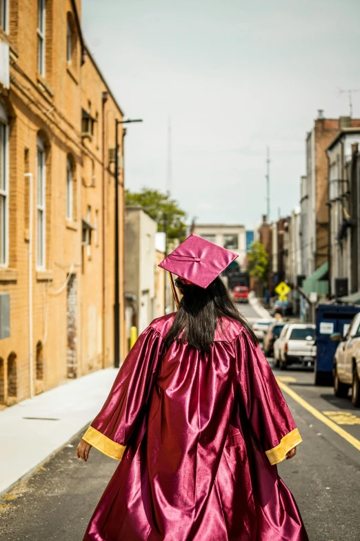 graduate walks away from the camera as she crosses the street