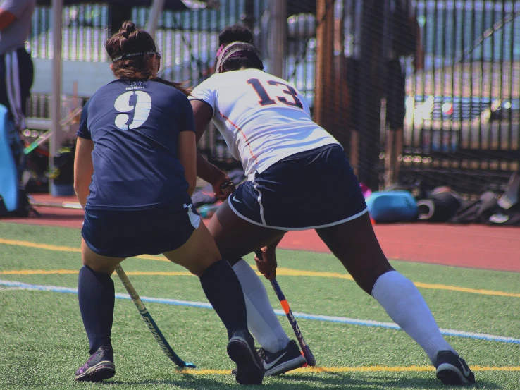 two girls playing field hockey while people watch from the stands