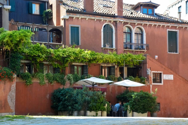 people are standing outside of an old building covered in green plants and umbrellas