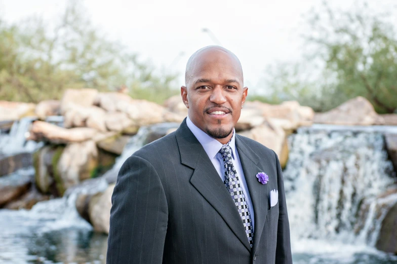 a man in a suit standing in front of a waterfall