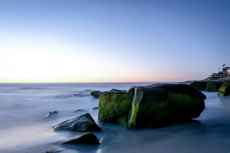 a long - exposure view of rocks and water from a beach