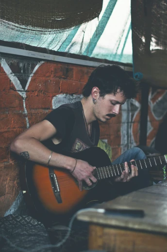 a man playing an electric guitar by a brick wall