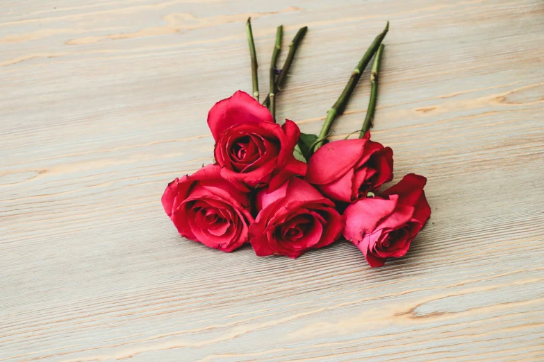 several red roses are placed on a wood table