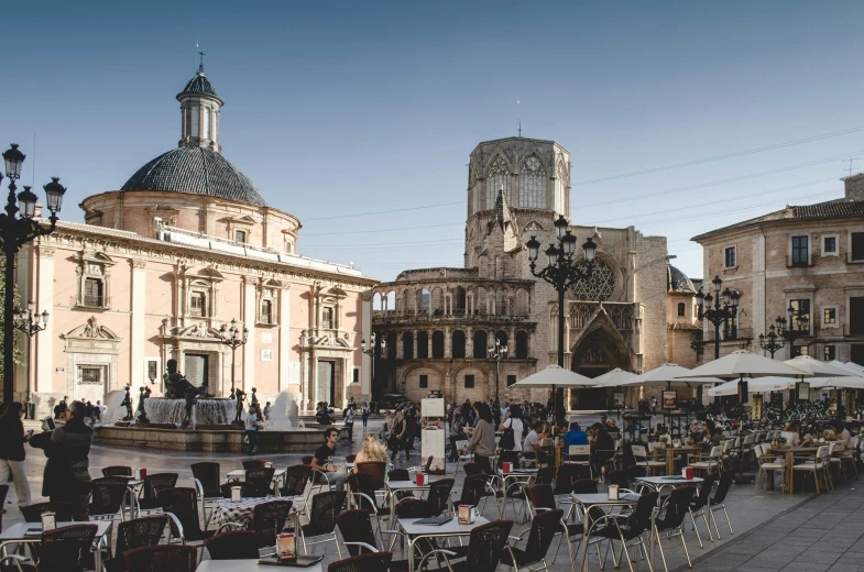 a view of an old european street with tables and chairs and some people