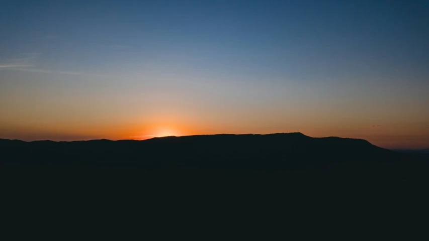 the sun is setting behind a hill covered in clouds