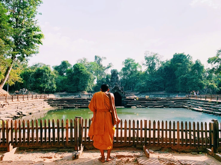 man in an orange robe standing by the pond