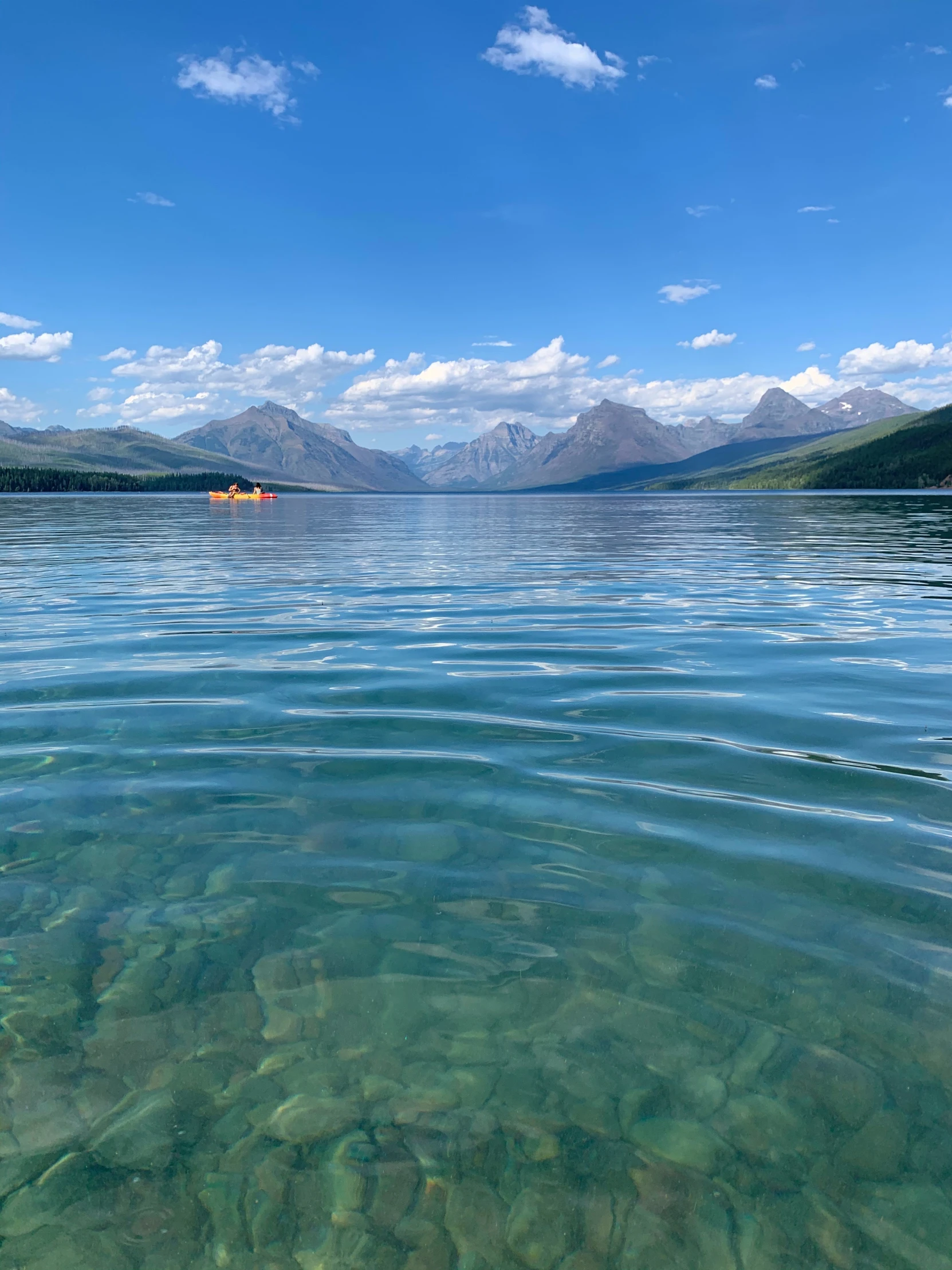 clear water with mountains and kayaks in the distance