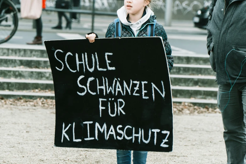 a small child holds a sign reading schle schwarznaffen fur klimaschutz