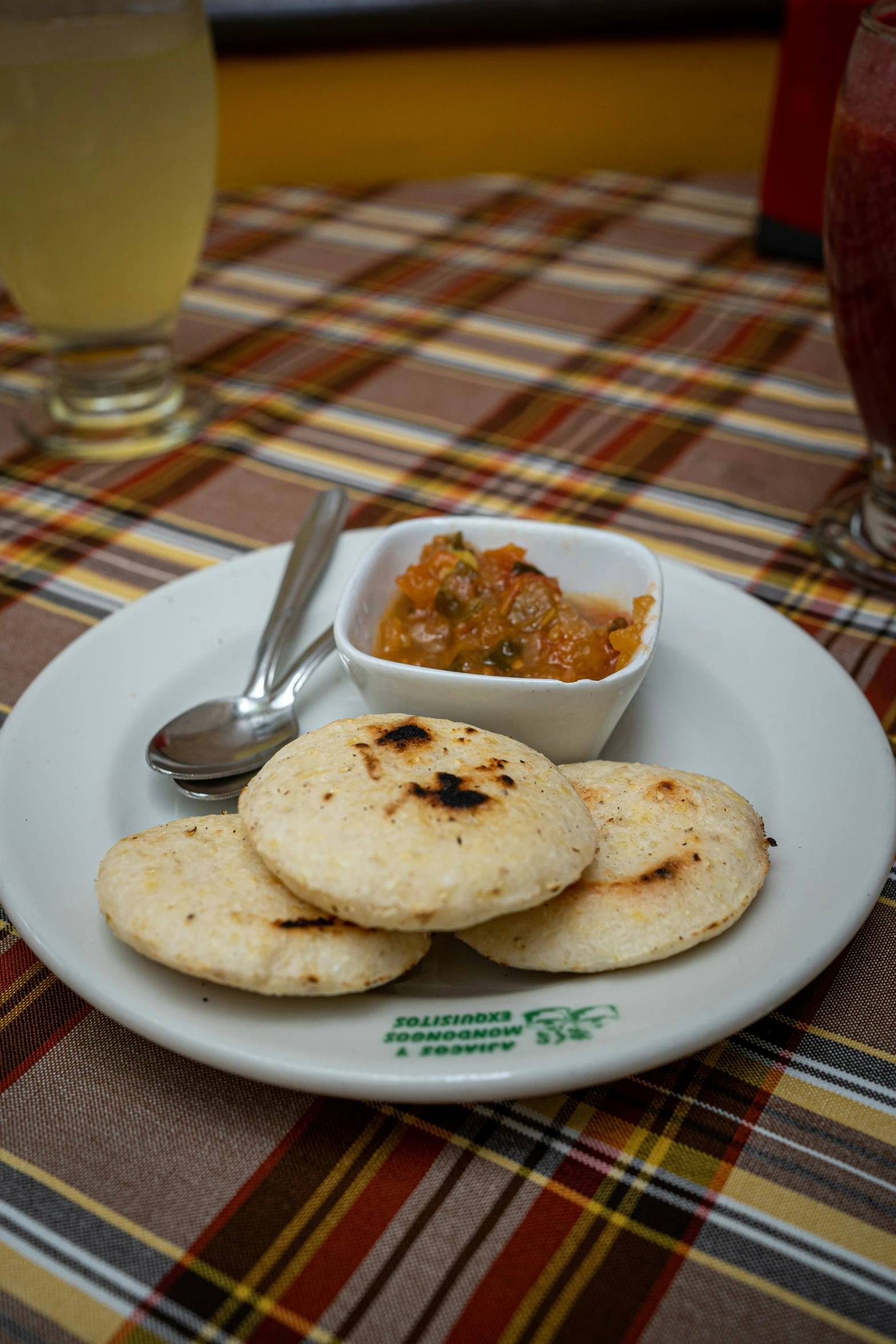 two small tortillas on a plate next to a bowl of salsa and spoon