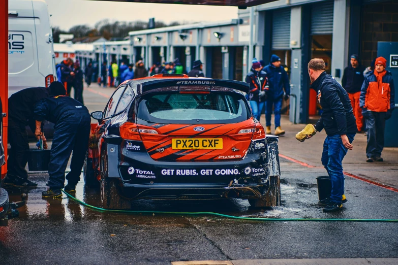 an orange van sits in the middle of a street as two men wash it