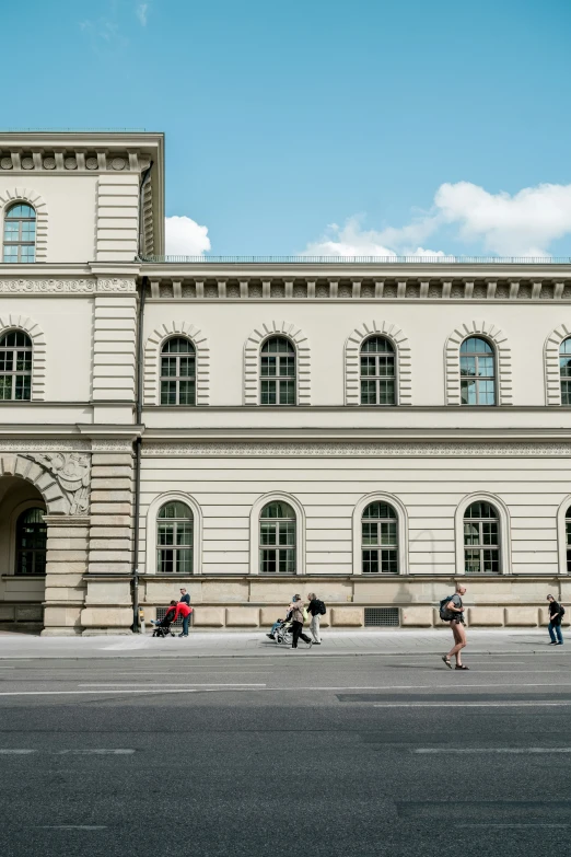 a long white building with several people walking around it