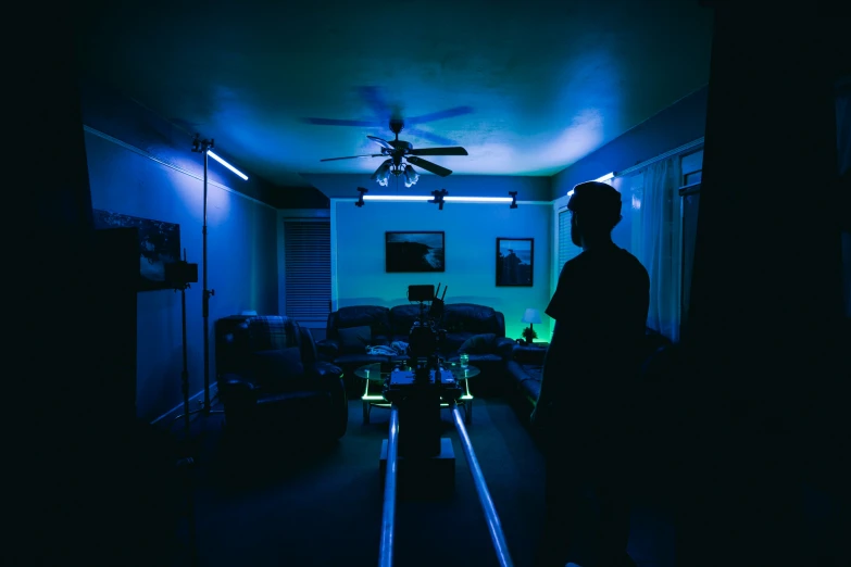 a man standing in a darkened room with a ceiling fan