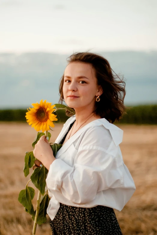 a woman standing in a field with a flower