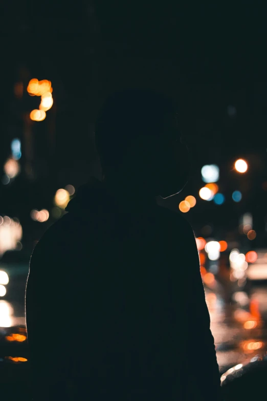 a silhouetted man standing next to a street at night