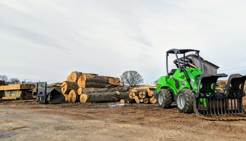 a green farm vehicle is parked by stacks of lumber