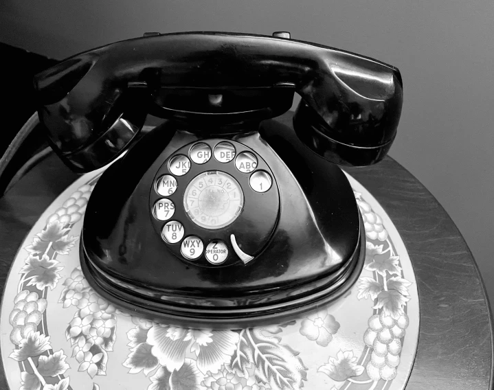 an old fashioned black rotary telephone sitting on a tray