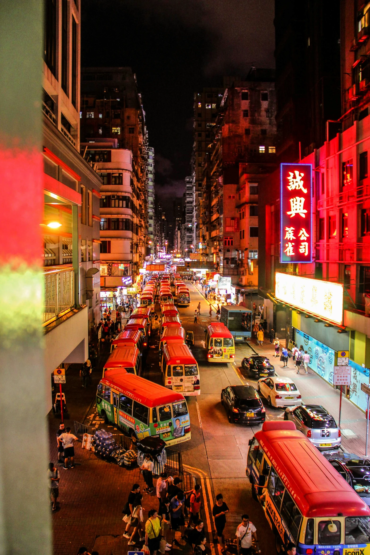 a crowded street filled with parked cars next to tall buildings