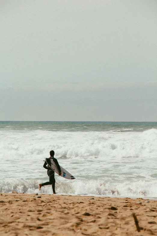 a man walks out from the ocean carrying a surfboard