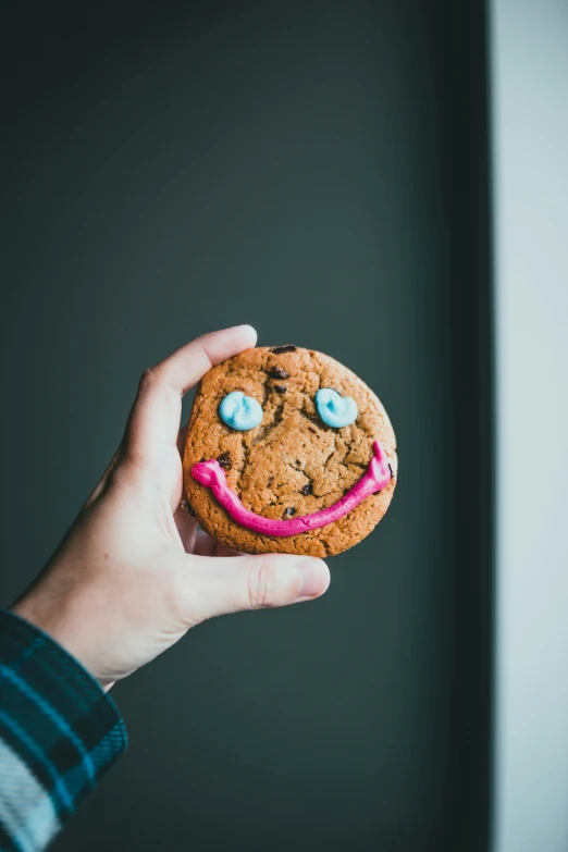 someone holding a chocolate chip cookie with a pink frosting