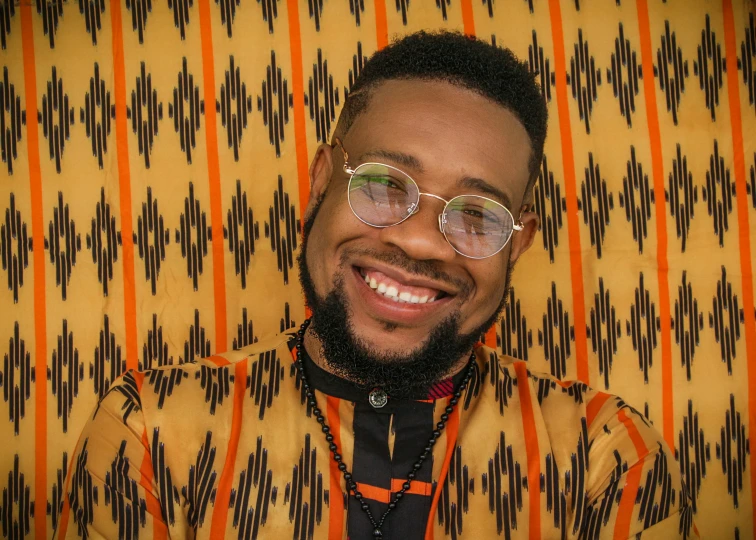 a man wearing glasses smiling with a colorful wall paper behind him