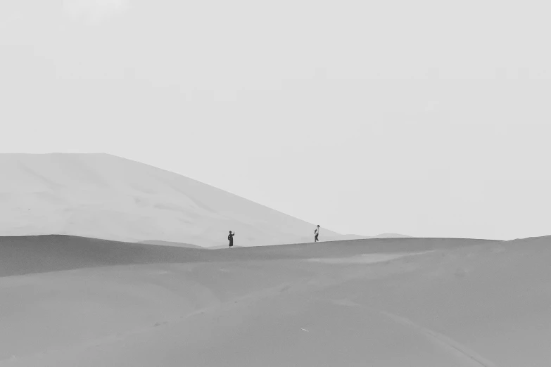two people walk across the desert sand dunes