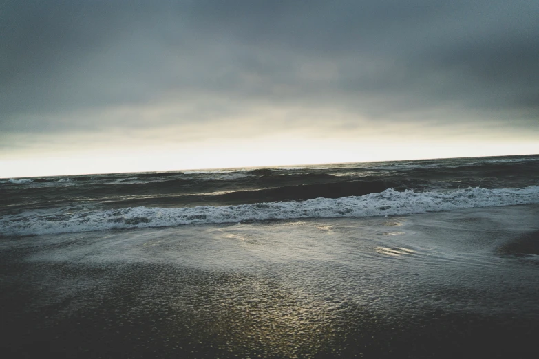 the ocean is near a sandy beach under a cloudy sky