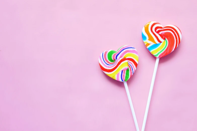 two lollipops with colorful frosting on them are on pink background