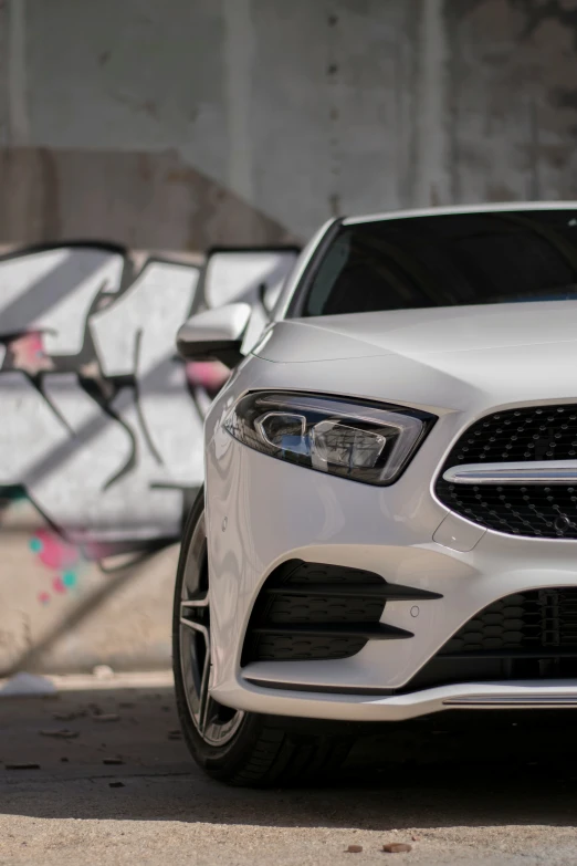 a white car sitting in front of graffiti on the wall