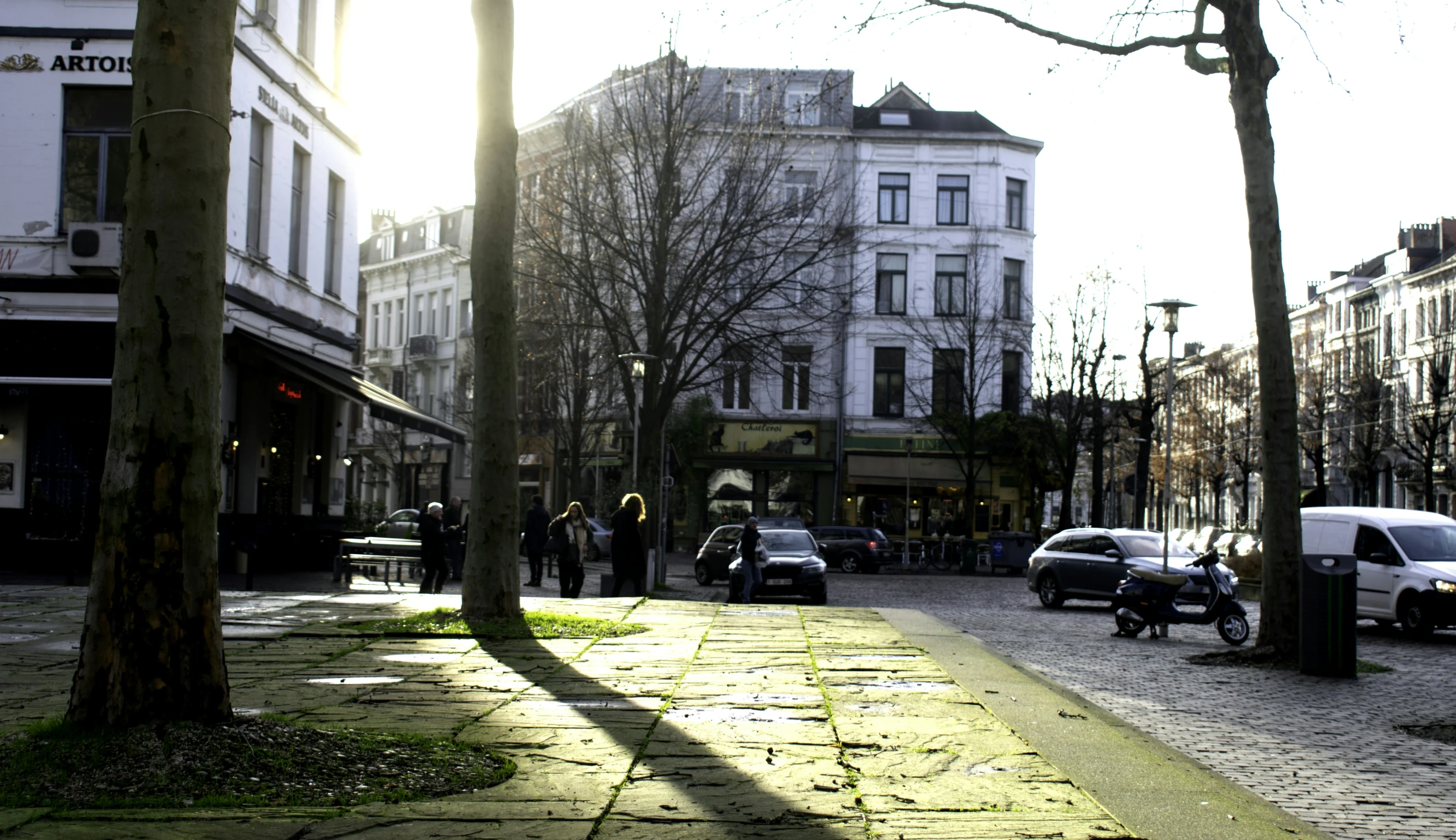 a busy sidewalk near several businesses with cars parked