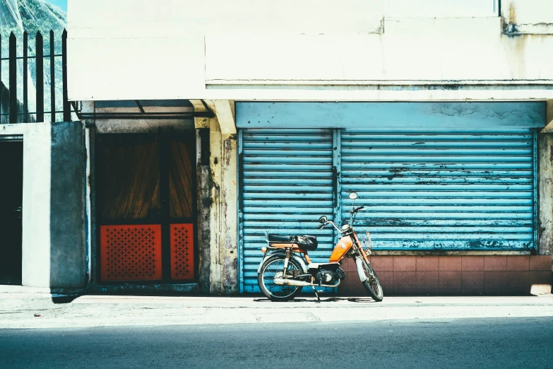 the orange motorcycle is parked on the street by the garage