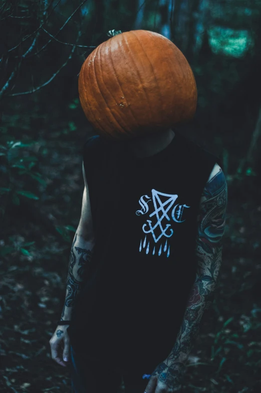 a man with a tattoo wearing a pumpkin hat in a forest