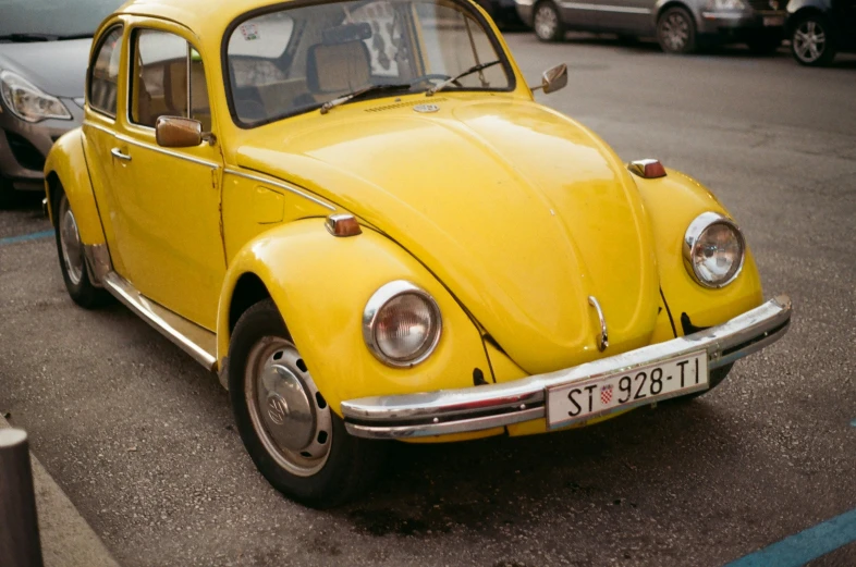 the front of a yellow vw bug parked next to a grey van