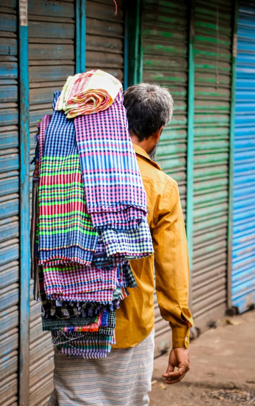 a man is carrying several pieces of clothing on his back