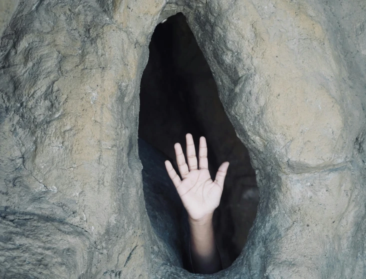 a hand sticking out from an area that has grey rocks and dirt