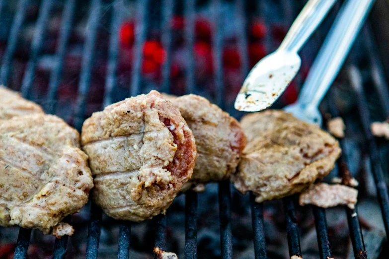 steaks are being grilled on a grill with tongs