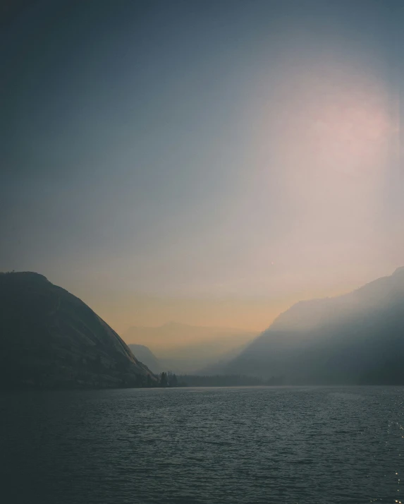 the sun is shining above a mountain, with a body of water in front