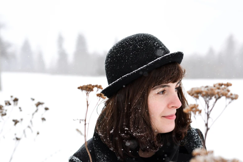 a young woman standing in snow with a hat on