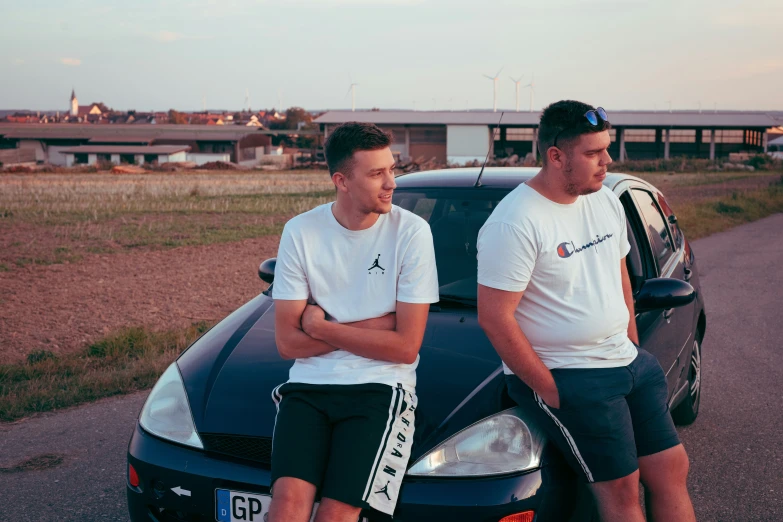 two young men are sitting on a car