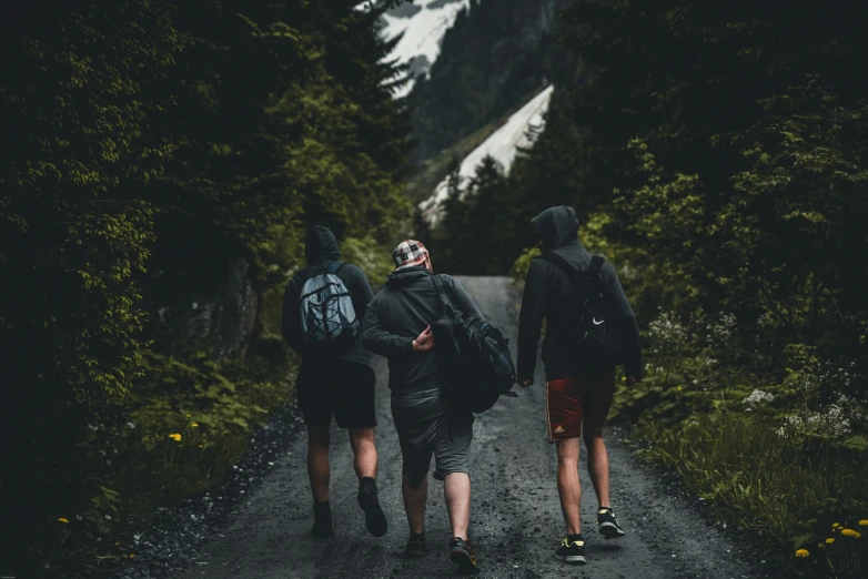 three people are walking down a road with backpacks